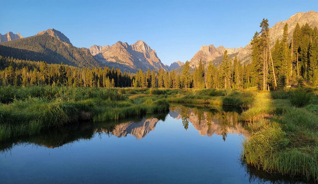 a view of the sawtooth mountains in idaho while hiking next to a reflective lake