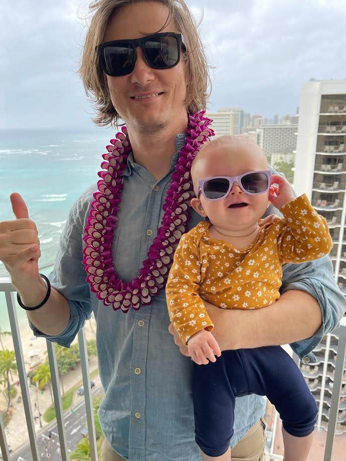 a man and his baby posing on the lanai overlooking waikiki beach from the twin fin hotel