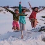 Three girls jump with excitement over white sand dunes in Africa