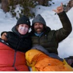 a father and daughter smile in their sleeping bags while camping
