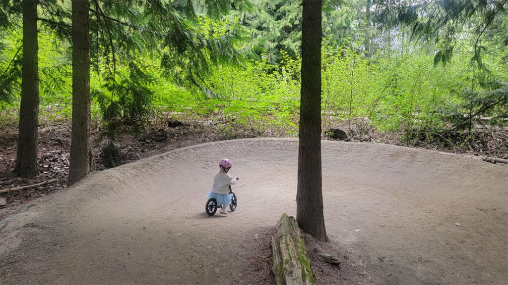 a young child rides around the corner of the hoods in the woods pump track in whistler british columbia