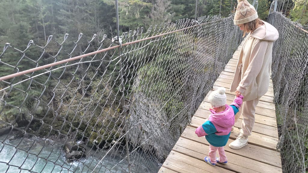 a mother and daughter cross a suspension bridge over the cheakamus river in the whistler interpretive forest