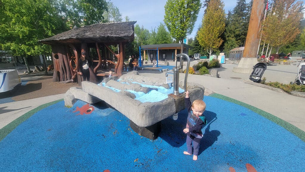a child plays in the water feature at the marketplace playground in whistler british columbia