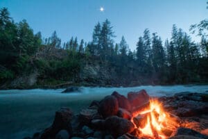 a campfire burns next to a river in whistler, british columbia, canada