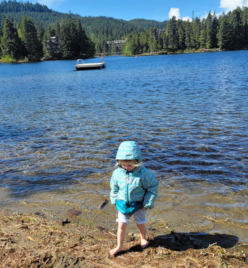a toddler wades on the beach at alpha lake park in whistler creekside, british columbia