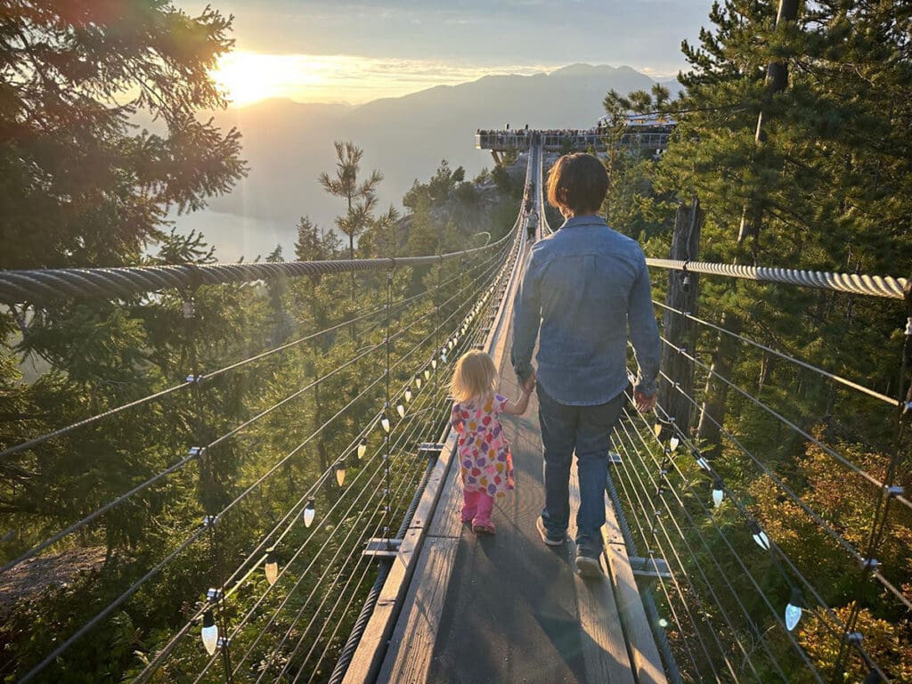 A father and daughter walk hand in hand on the skypilot suspension bridge at the sea to sky gondola