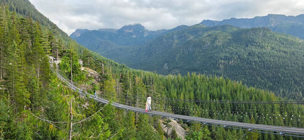 a mother and daughter walk across the suspension bridge at the sea to sky gondola