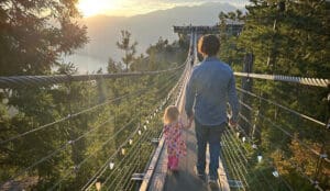 a father and daughter walk across the skypilot suspension bridge at the sea to sky gondola during golden hour