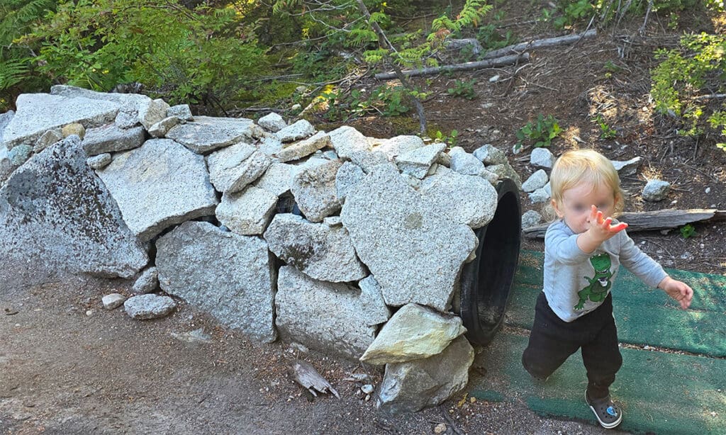 a small child emerges from a tunnel decorated with rocks on the alpine alley trail on the sea to sky gondola