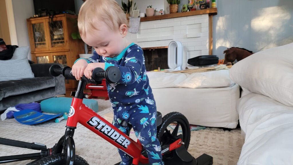a baby steps onto a balance bike for the first time in their living room