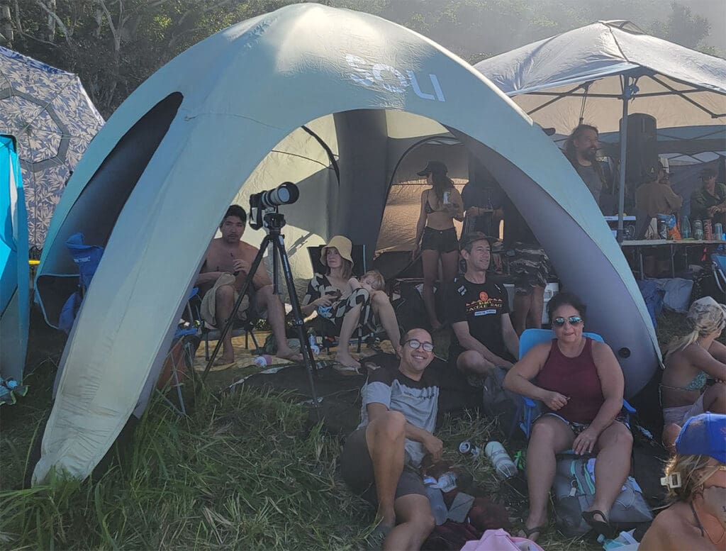 a shade canopy filled with people during the eddie aikau surfing event at waimea bay, hawaii