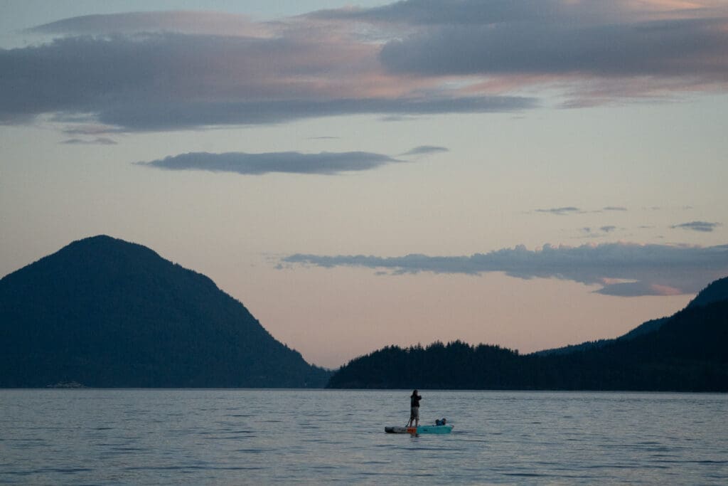 a woman paddleboards at sunset with her children on the bow
