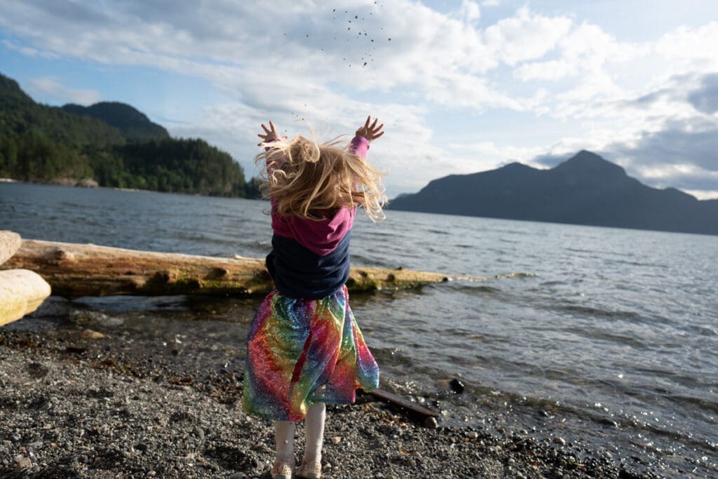 a girl throws rocks into the ocean at howe sound, british columbia