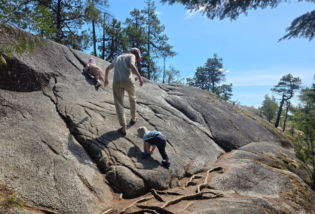 a mother hikes on a large granit rock with her two young toddlers in murrin provincial park near squaish bc