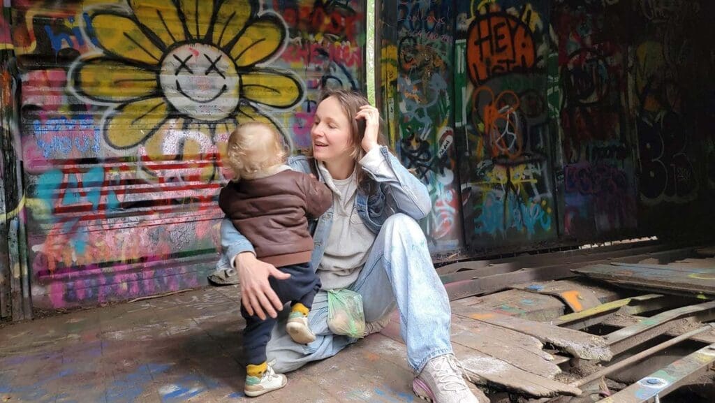 a mom and baby play together inside a graffiti-laden boxcar on the train wreck trail in whistler, BC, Canada
