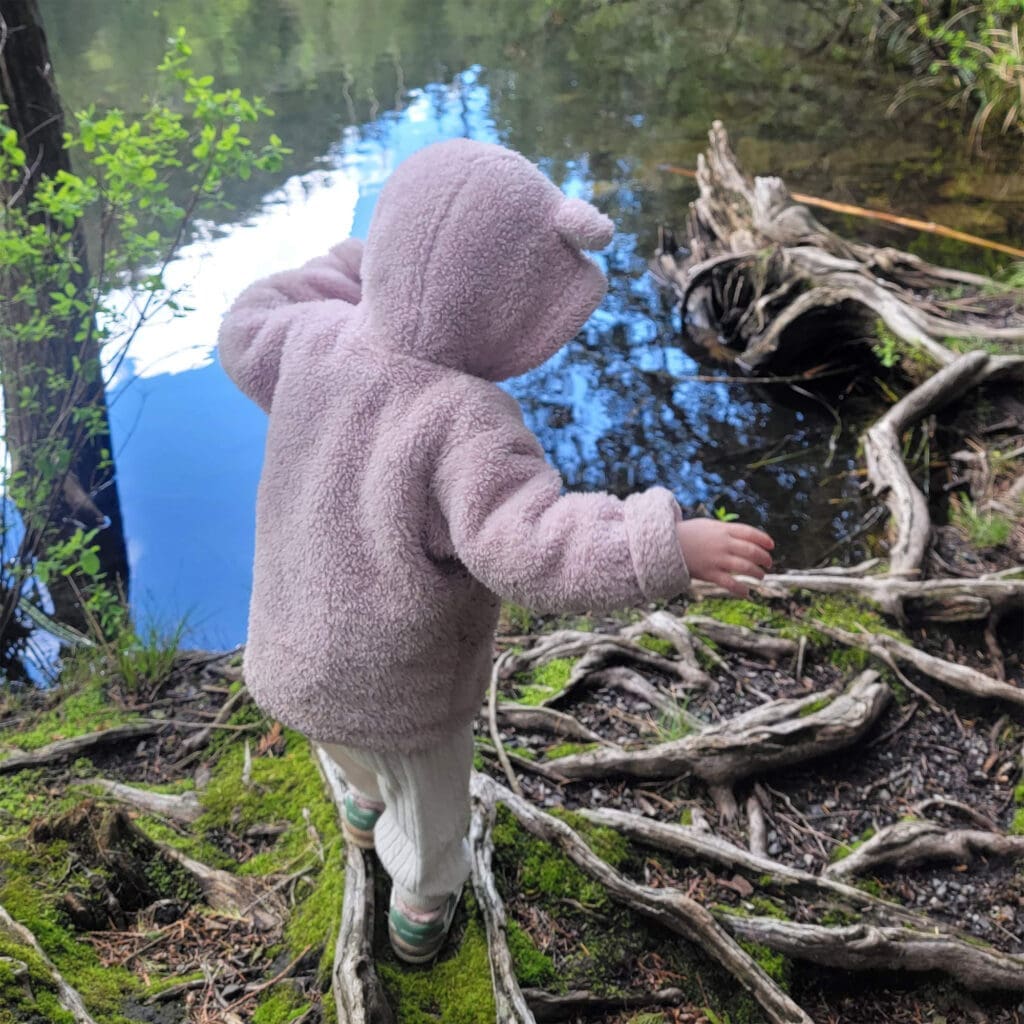 a young toddler balances on a log next to Browning lake in Murrin park, British Columbia, Canada