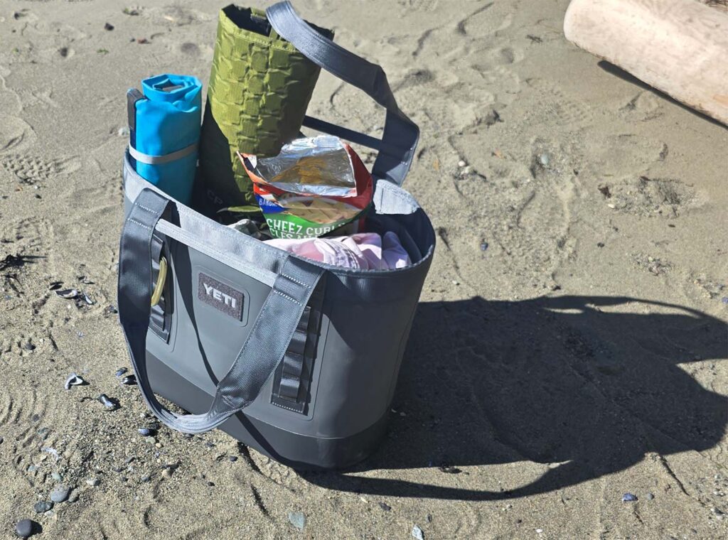 a yeti camino 35 tote stands upright on the sand during a beach outing.