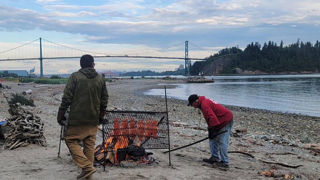 two men cook salmon over the fire at ambleside beach in vancouver bc